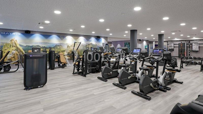 Salle de sport équipée de vélos d'appartement, machines de musculation et autres équipements modernes.