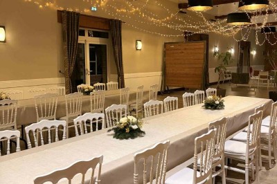 Des personnes discutent debout autour de tables en bois devant des tentes blanches dans un espace extérieur arboré.