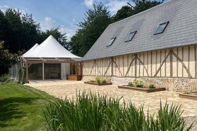 Des personnes discutent debout autour de tables en bois devant des tentes blanches dans un espace extérieur arboré.