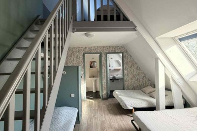 Des personnes discutent debout autour de tables en bois devant des tentes blanches dans un espace extérieur arboré.