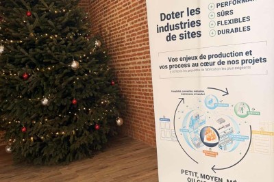 Des personnes discutent debout autour de tables en bois devant des tentes blanches dans un espace extérieur arboré.