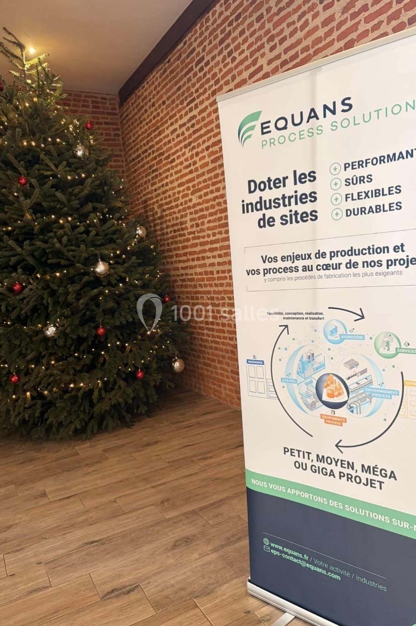 Bannière d'entreprise devant un sapin de Noël décoré, dans un espace intérieur aux murs en briques.
