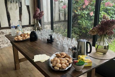 Des personnes discutent debout autour de tables en bois devant des tentes blanches dans un espace extérieur arboré.