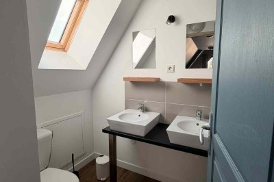 Des personnes discutent debout autour de tables en bois devant des tentes blanches dans un espace extérieur arboré.