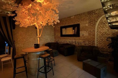 Des personnes discutent debout autour de tables en bois devant des tentes blanches dans un espace extérieur arboré.