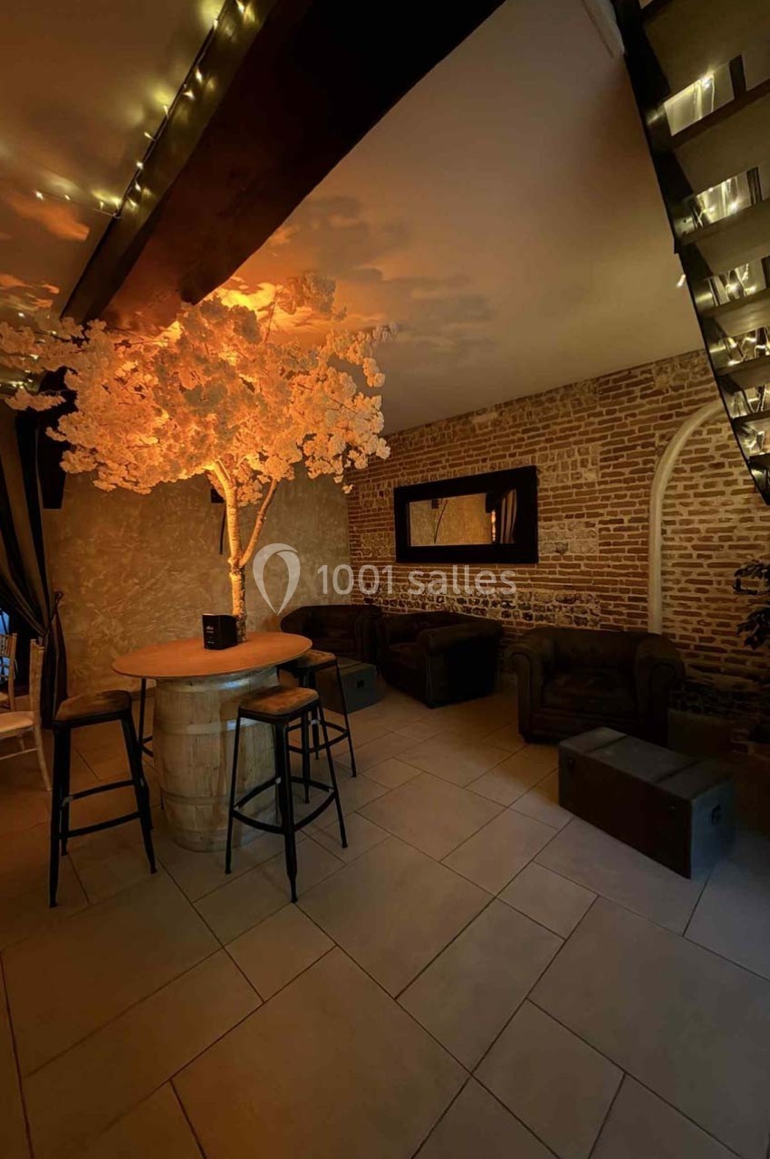 Espace intérieur avec un arbre lumineux décoratif, des fauteuils en cuir, un mur en briques et un bar en tonneau.