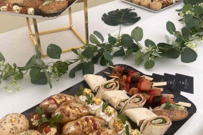 Des personnes discutent debout autour de tables en bois devant des tentes blanches dans un espace extérieur arboré.