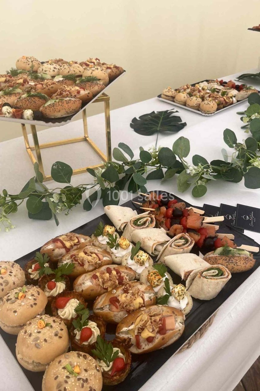 Plateaux de bouchées salées variées disposés sur une table décorée de feuillage vert.
