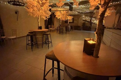 Des personnes discutent debout autour de tables en bois devant des tentes blanches dans un espace extérieur arboré.