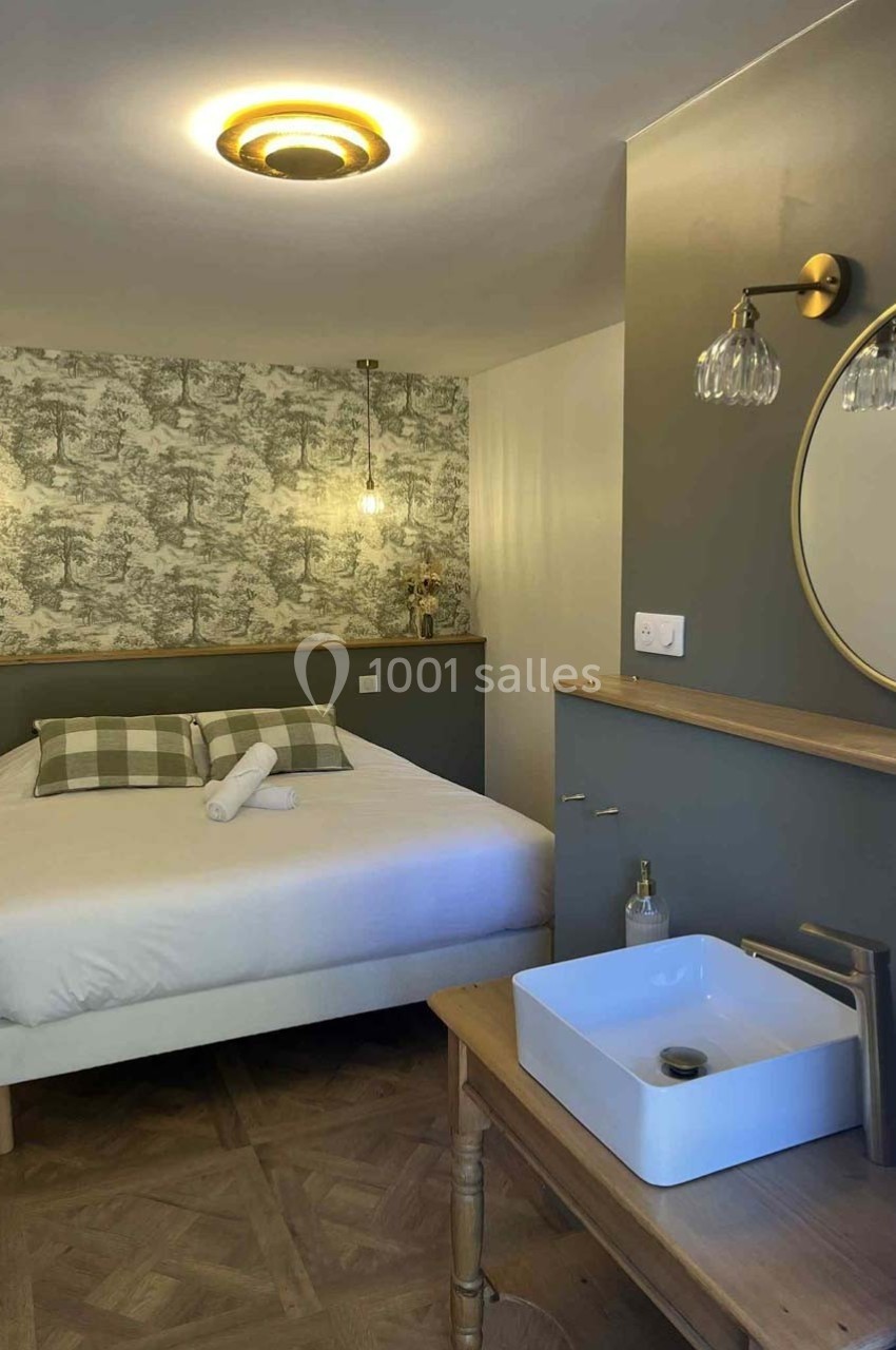 Chambre avec lit double, mur décoré de papier peint, lavabo sur meuble en bois et éclairage chaleureux.