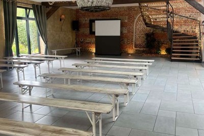 Des personnes discutent debout autour de tables en bois devant des tentes blanches dans un espace extérieur arboré.