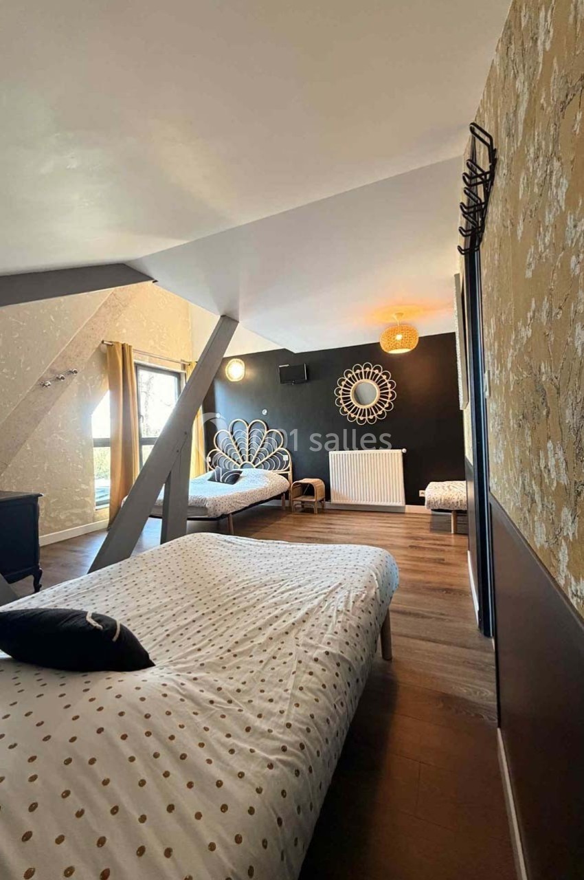 Chambre mansardée avec trois lits, parquet, murs décorés et grande fenêtre laissant entrer la lumière naturelle.