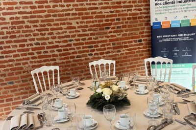 Des personnes discutent debout autour de tables en bois devant des tentes blanches dans un espace extérieur arboré.