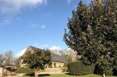 Des personnes discutent debout autour de tables en bois devant des tentes blanches dans un espace extérieur arboré.