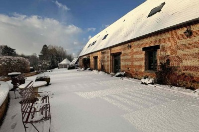 Des personnes discutent debout autour de tables en bois devant des tentes blanches dans un espace extérieur arboré.