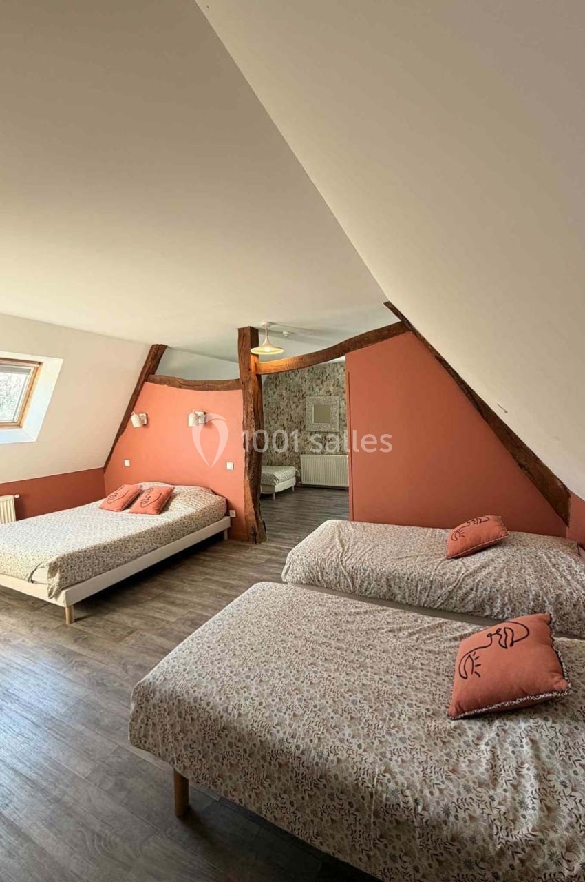 Chambre mansardée avec deux lits simples et un lit double, murs roses et poutres apparentes, parquet au sol.