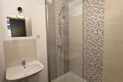 Des personnes discutent debout autour de tables en bois devant des tentes blanches dans un espace extérieur arboré.