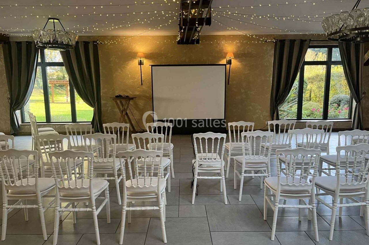 Salle de réunion avec des chaises blanches alignées face à un écran de projection, éclairée par des guirlandes lumineuses.