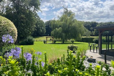 Des personnes discutent debout autour de tables en bois devant des tentes blanches dans un espace extérieur arboré.