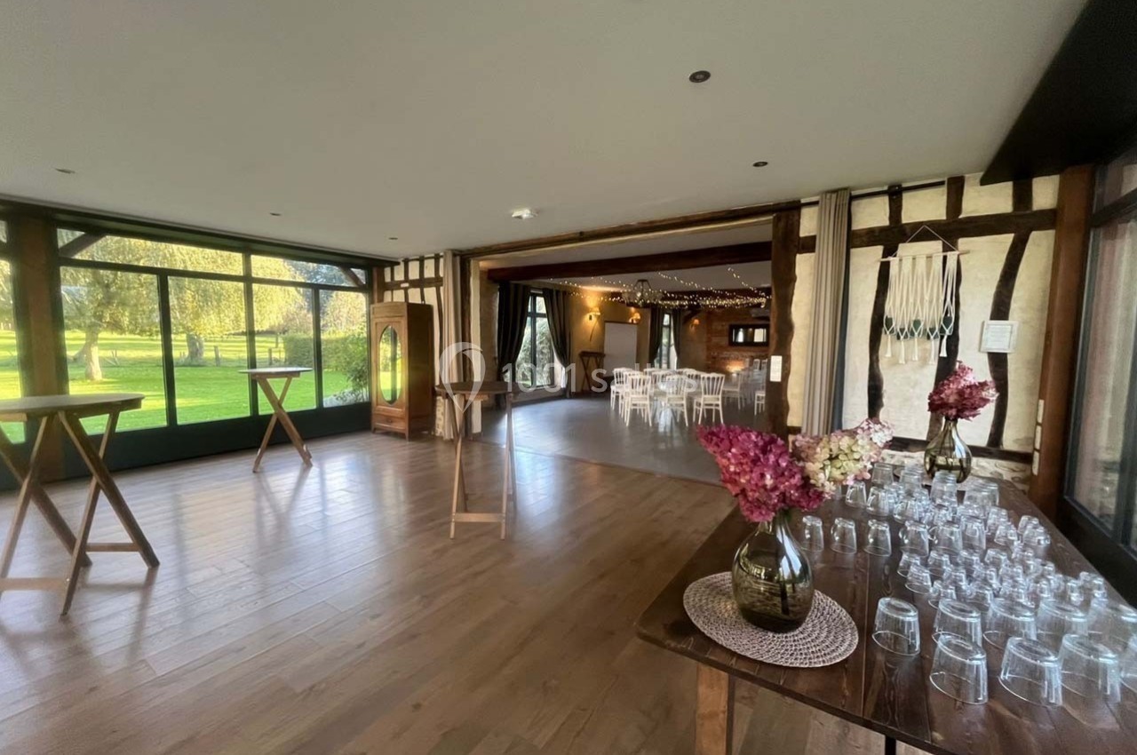 Salle lumineuse avec parquet, tables en bois, décorations florales et baies vitrées donnant sur un espace extérieur…