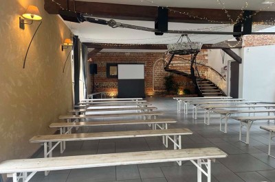 Des personnes discutent debout autour de tables en bois devant des tentes blanches dans un espace extérieur arboré.