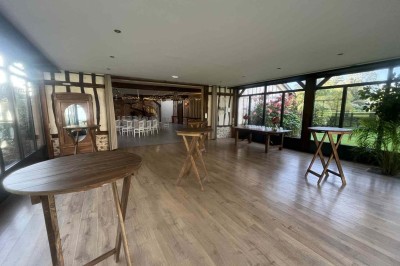 Des personnes discutent debout autour de tables en bois devant des tentes blanches dans un espace extérieur arboré.