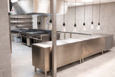 Cuisine professionnelle moderne avec équipements en inox, éclairage suspendu et fourneaux sous une hotte d'extraction.