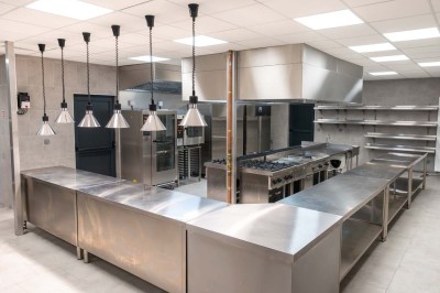 Cuisine professionnelle moderne avec équipements en inox, éclairage suspendu et fourneaux sous une hotte d'extraction.