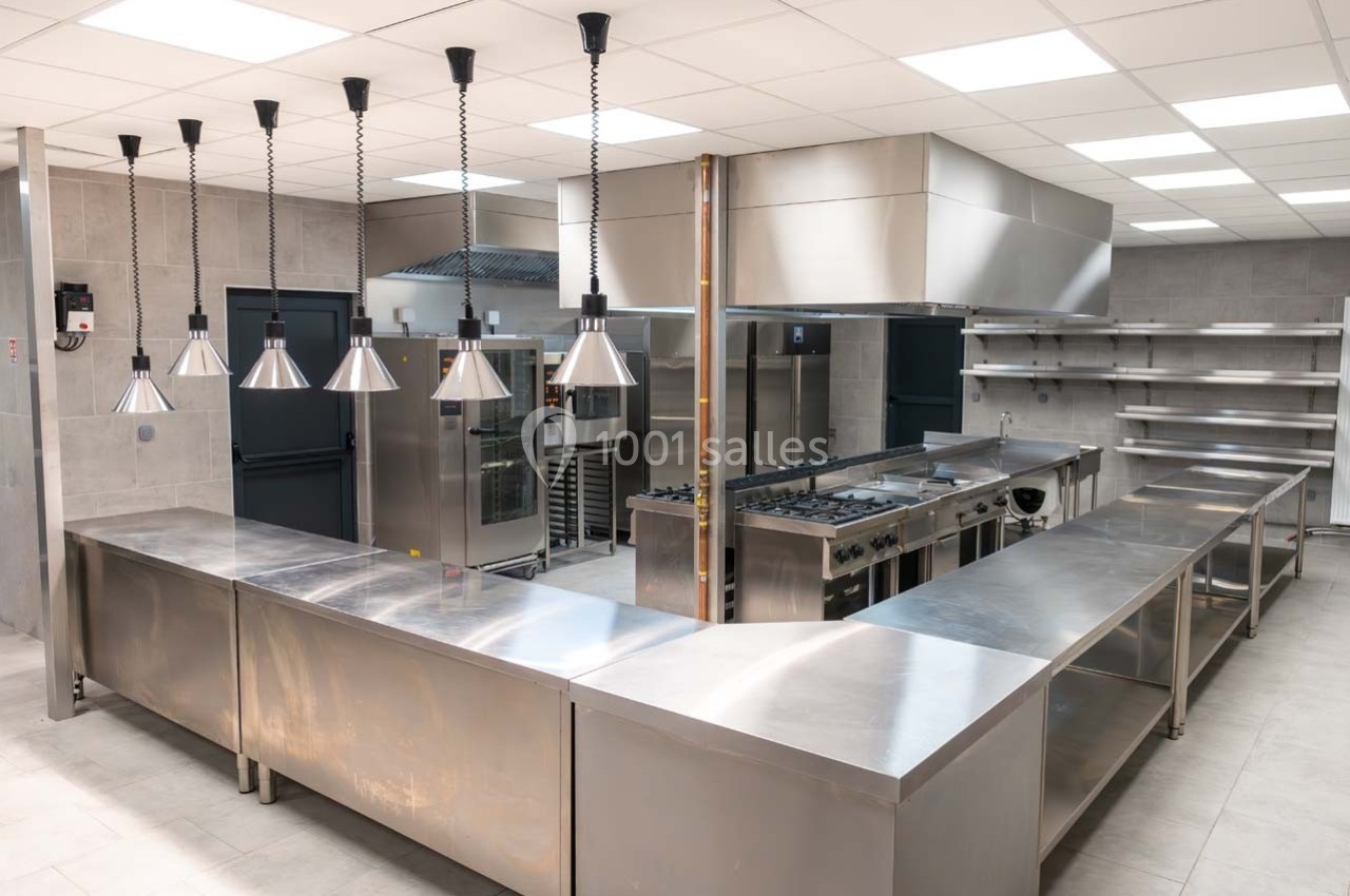 Cuisine professionnelle moderne avec plans de travail en inox, équipements de cuisson et éclairage suspendu.