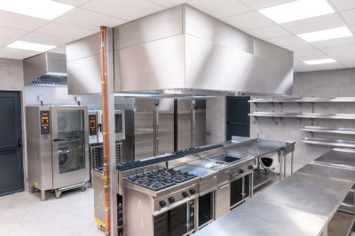 Cuisine professionnelle moderne avec équipements en inox, éclairage suspendu et fourneaux sous une hotte d'extraction.