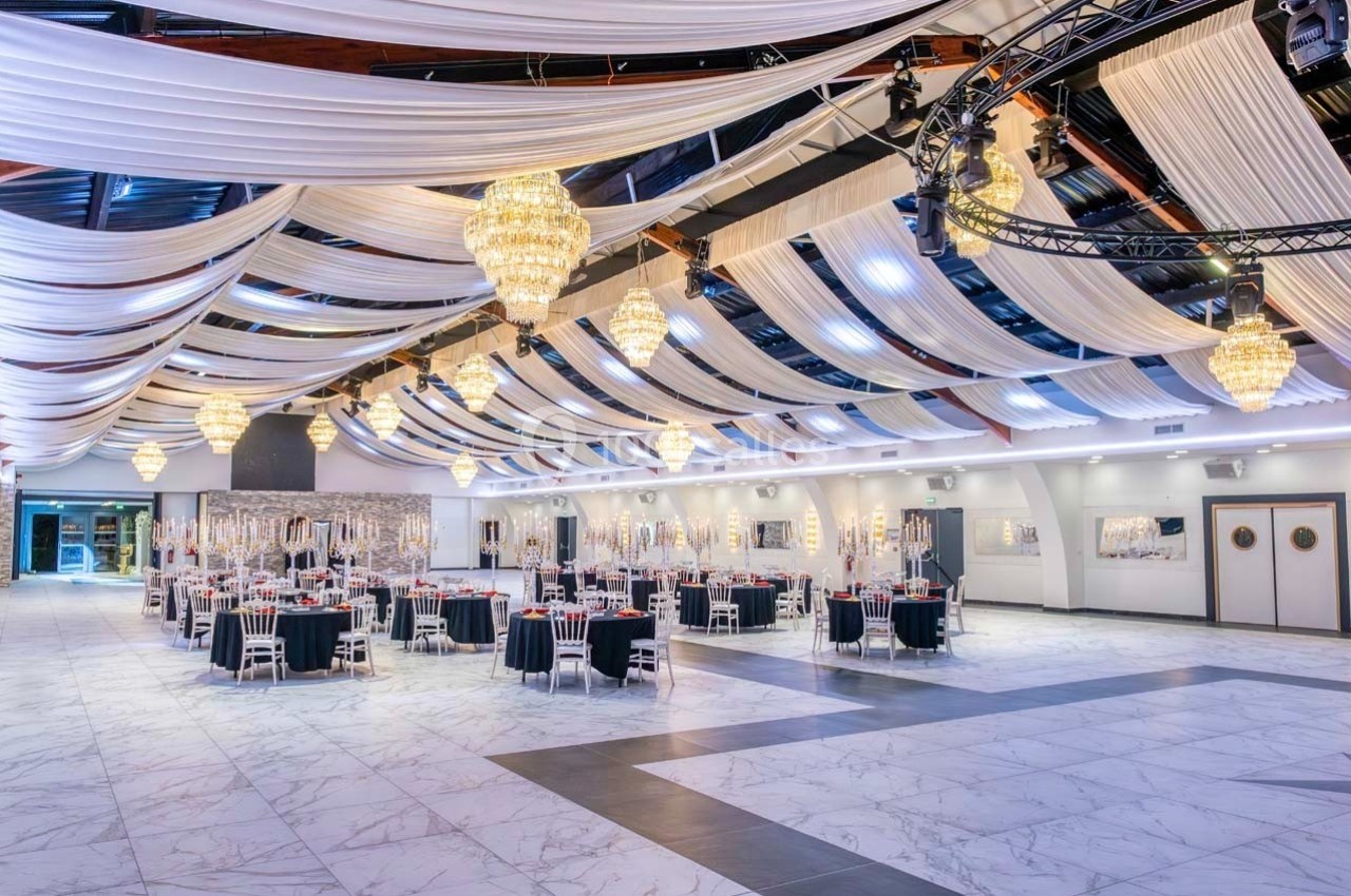 Grande salle de réception décorée avec des lustres, des drapés blancs au plafond et des tables dressées élégamment.