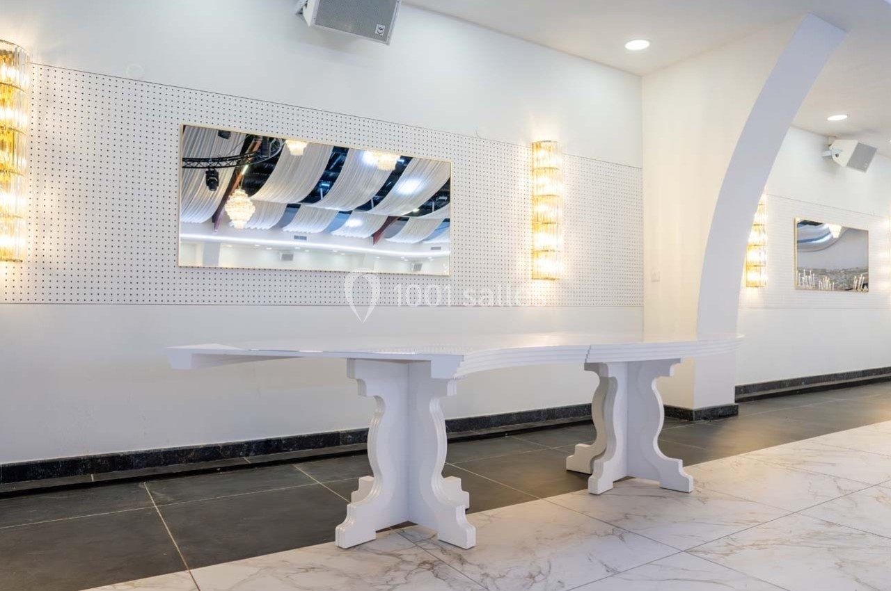 Table blanche moderne dans une pièce lumineuse avec un mur perforé, des miroirs et des appliques murales.