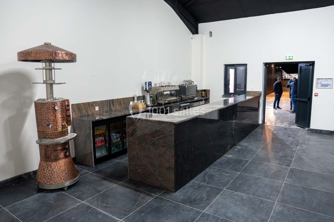 Comptoir de bar moderne en marbre sombre avec équipements, réfrigérateurs et un chauffe-plat en cuivre à gauche.