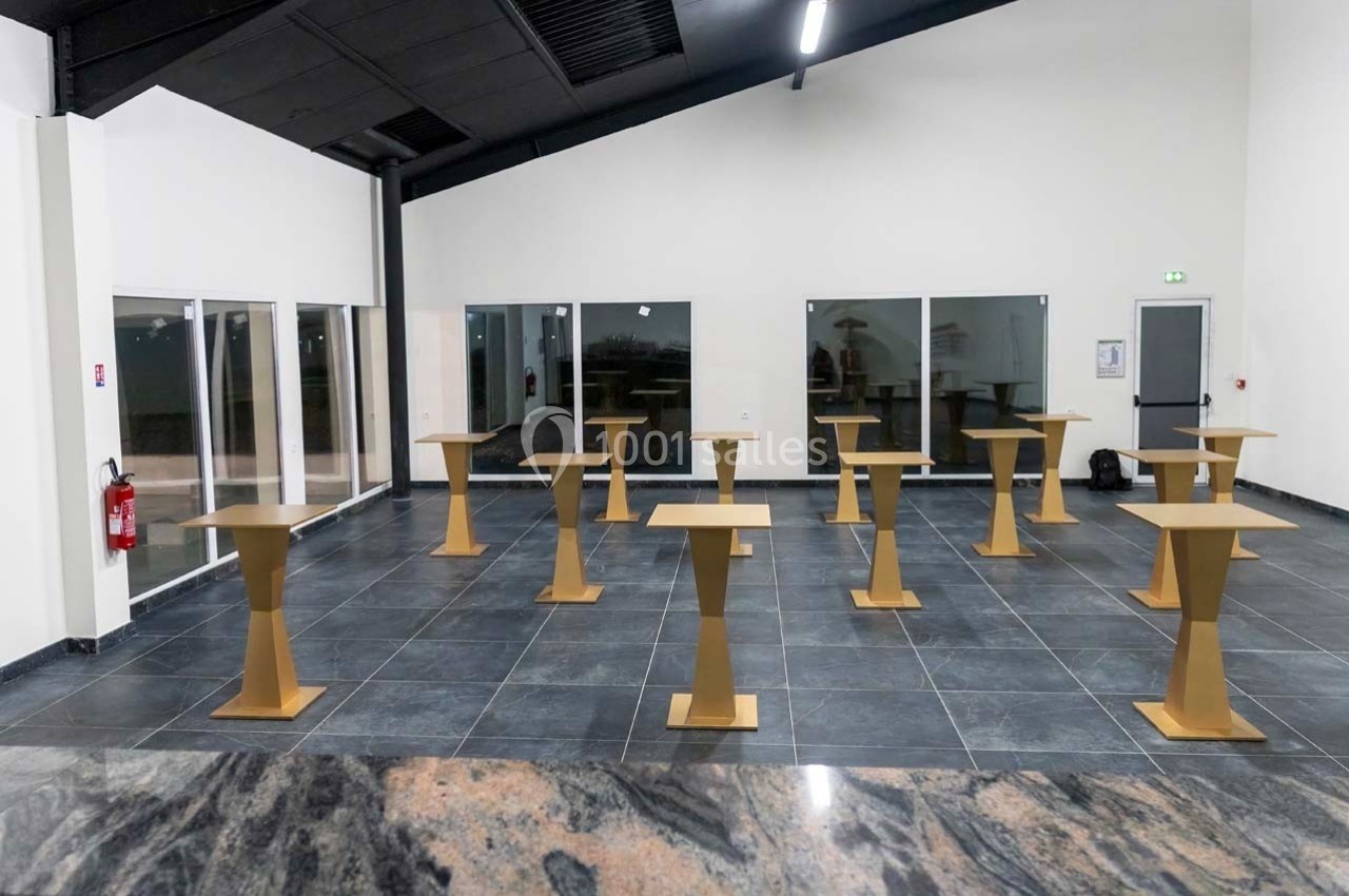 Salle avec sol en carrelage sombre, plusieurs pupitres dorés espacés et grandes baies vitrées en arrière-plan.