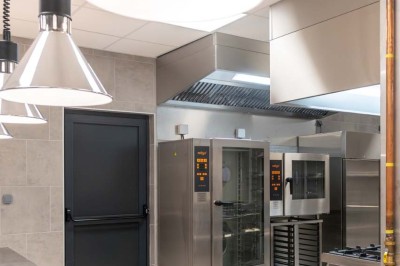 Cuisine professionnelle moderne avec équipements en inox, éclairage suspendu et fourneaux sous une hotte d'extraction.