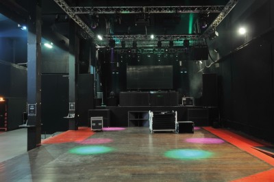 Foule dans une salle sombre éclairée par des lumières rouges intenses, avec une scène visible au fond.