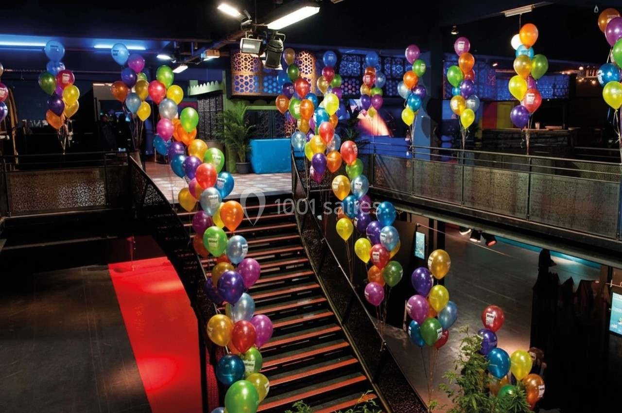 Escalier décoré de ballons multicolores dans une grande salle sombre avec éclairage tamisé.