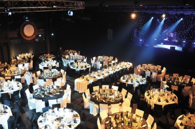 Foule dans une salle sombre éclairée par des lumières rouges intenses, avec une scène visible au fond.