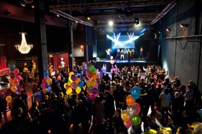 Foule dans une salle sombre éclairée par des lumières rouges intenses, avec une scène visible au fond.