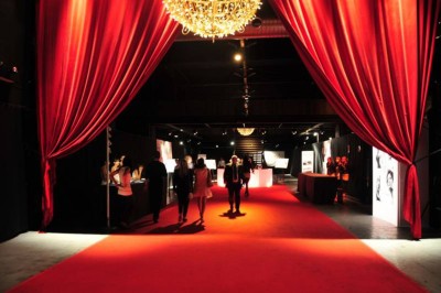 Foule dans une salle sombre éclairée par des lumières rouges intenses, avec une scène visible au fond.