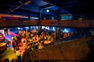 Foule dans une salle sombre éclairée par des lumières rouges intenses, avec une scène visible au fond.