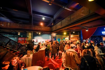 Foule dans une salle sombre éclairée par des lumières rouges intenses, avec une scène visible au fond.