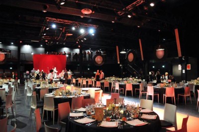 Foule dans une salle sombre éclairée par des lumières rouges intenses, avec une scène visible au fond.