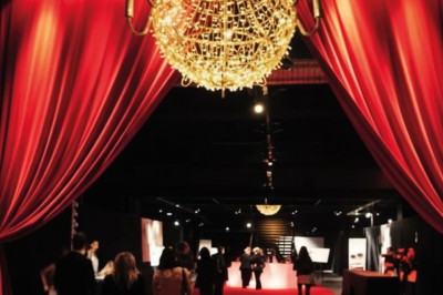 Foule dans une salle sombre éclairée par des lumières rouges intenses, avec une scène visible au fond.