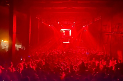Foule dans une salle sombre éclairée par des lumières rouges intenses, avec une scène visible au fond.