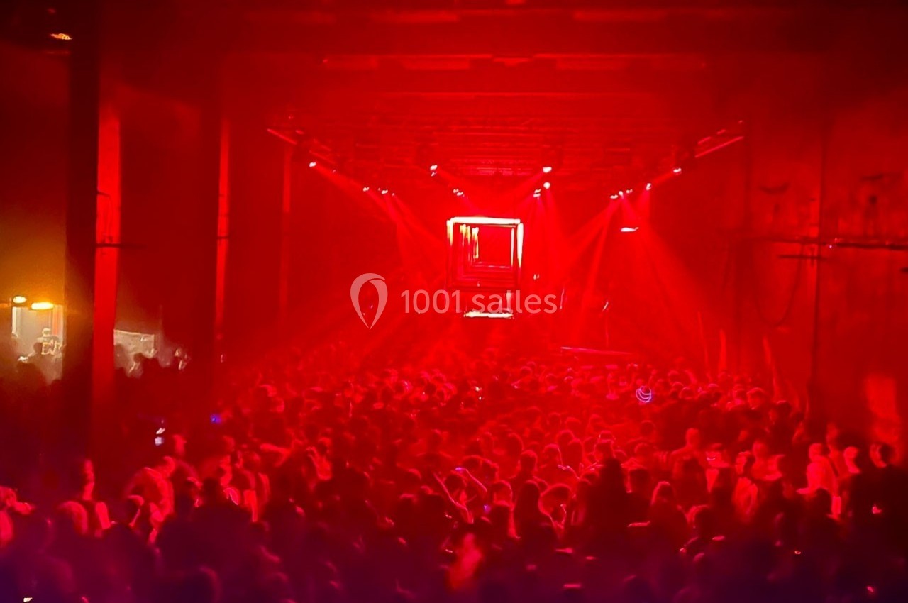 Foule dans une salle sombre éclairée par des lumières rouges intenses, avec une scène visible au fond.