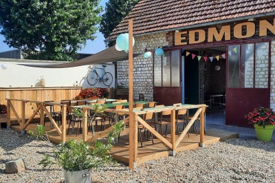 Terrasse aménagée avec tables, chaises et parasols devant une maison en pierre, entourée de verdure.