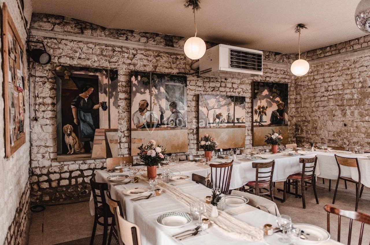 Salle de restaurant avec murs en pierre, tables dressées et décorations florales, ornée de peintures murales colorées.