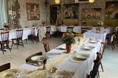 Terrasse aménagée avec tables, chaises et parasols devant une maison en pierre, entourée de verdure.
