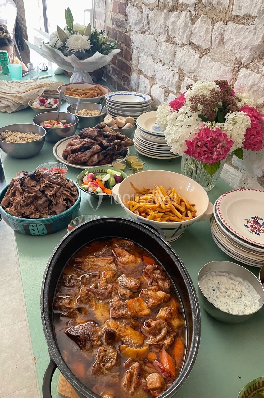 Buffet avec plats variés : viande en sauce, frites, légumes, riz, pain, crudités, et bouquets de fleurs en arrière-plan.